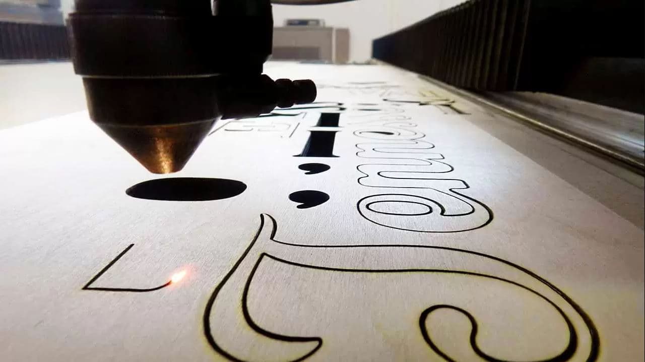 Dettaglio di lavorazione CNC su legno con incisione di caratteri tipografici tramite testa laser