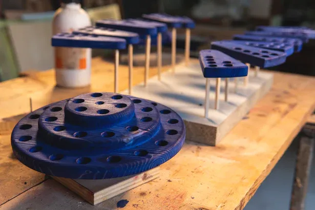 Componenti in legno verniciato blu realizzati con pantografo CNC, in fase di asciugatura su banco da lavoro artigianale.webp